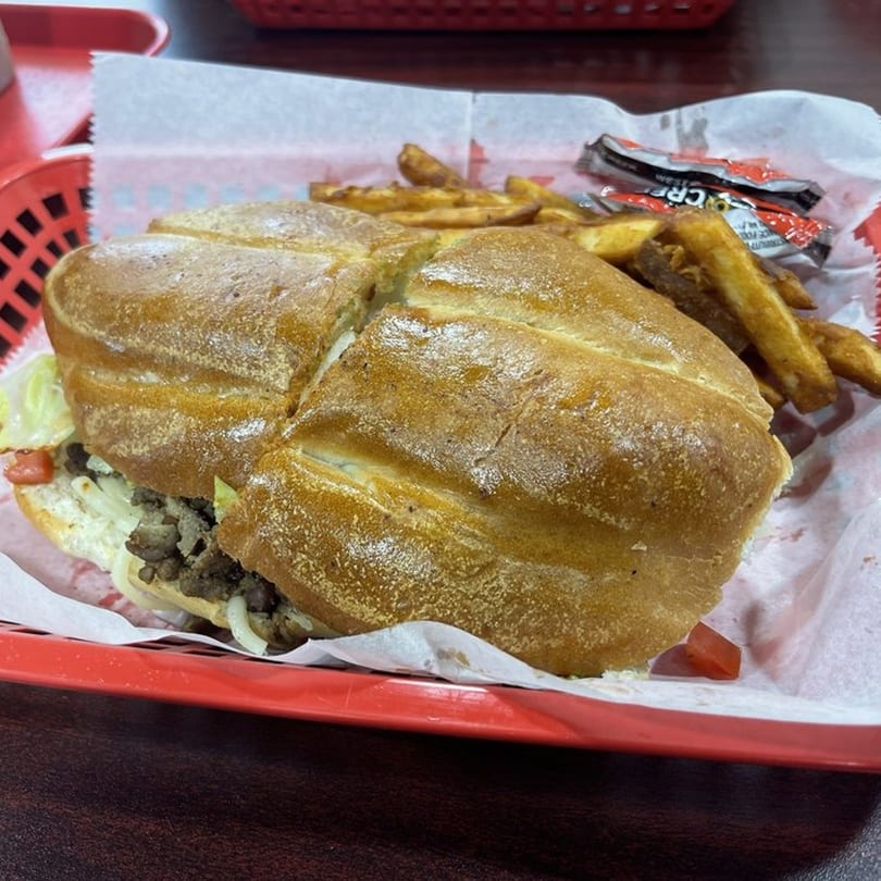 A Sazón Bello Taquería torta with fries and sauce packets in a red basket.