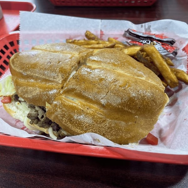 A Sazón Bello Taquería torta with steak, lettuce, and onions, served with fries in a red basket.