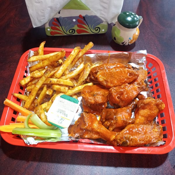 A red basket of Sazón Bello Taquería's buffalo wings, fries, celery, carrots, and ranch dressing.