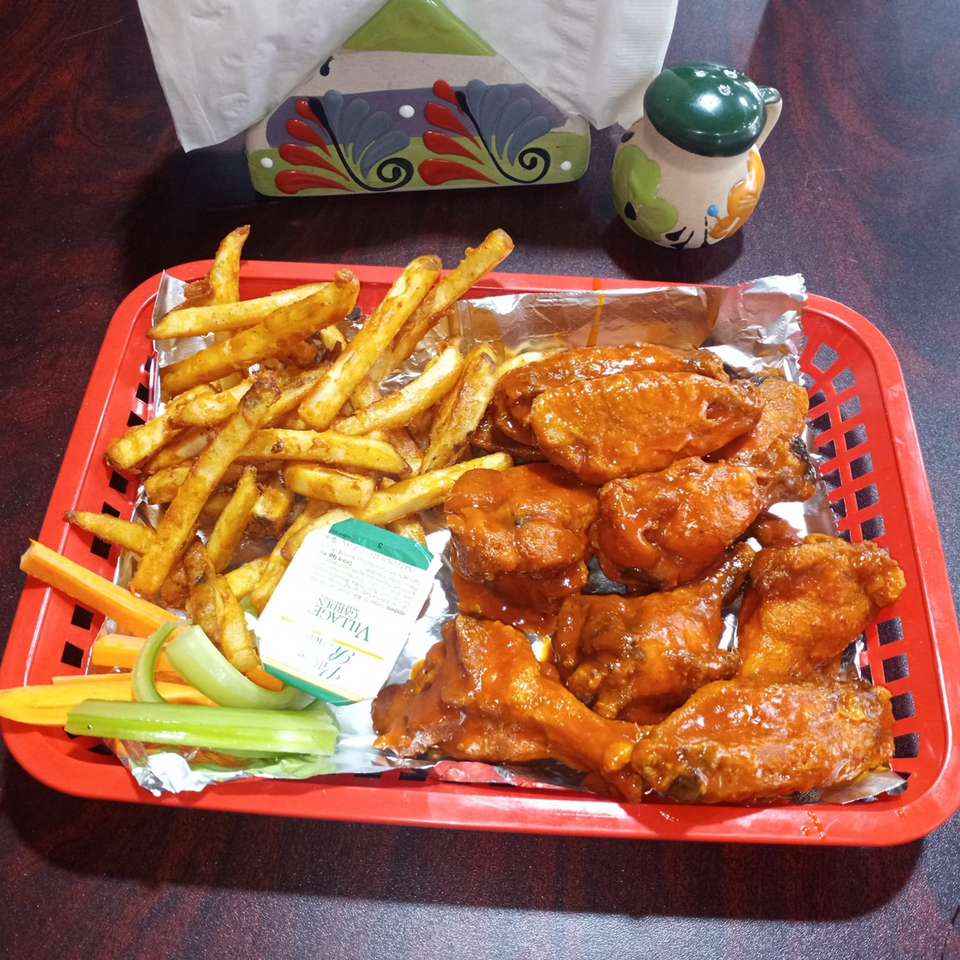A red basket of Sazón Bello Taquería's buffalo wings, fries, celery, carrots, and ranch dressing.