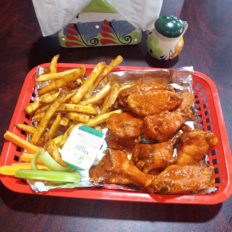 Sazón Bello Taquería's buffalo wings and fries in a red basket with celery, carrots, and ranch.