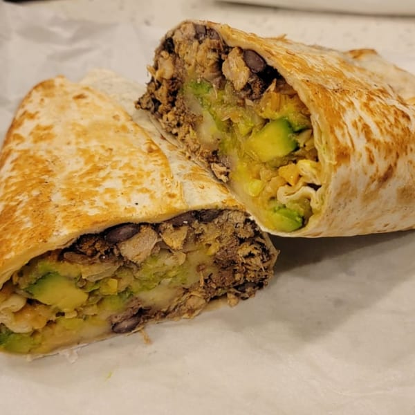 A Sazón Bello Taquería burrito, cut in half, revealing chicken, black beans, and avocado.