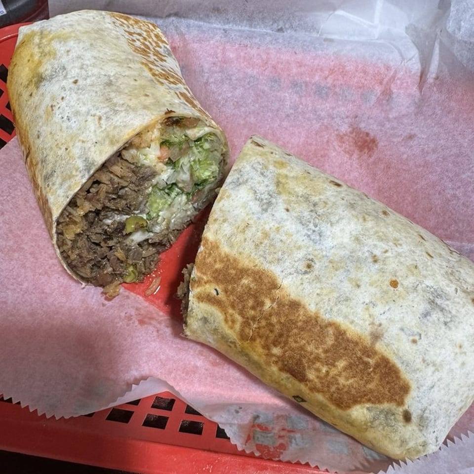 A large Sazón Bello Taquería burrito, cut in half, revealing meat, avocado, and other fillings.